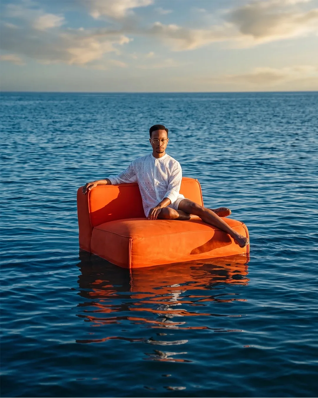 Retrato editorial en un sofá naranja flotando en el mar