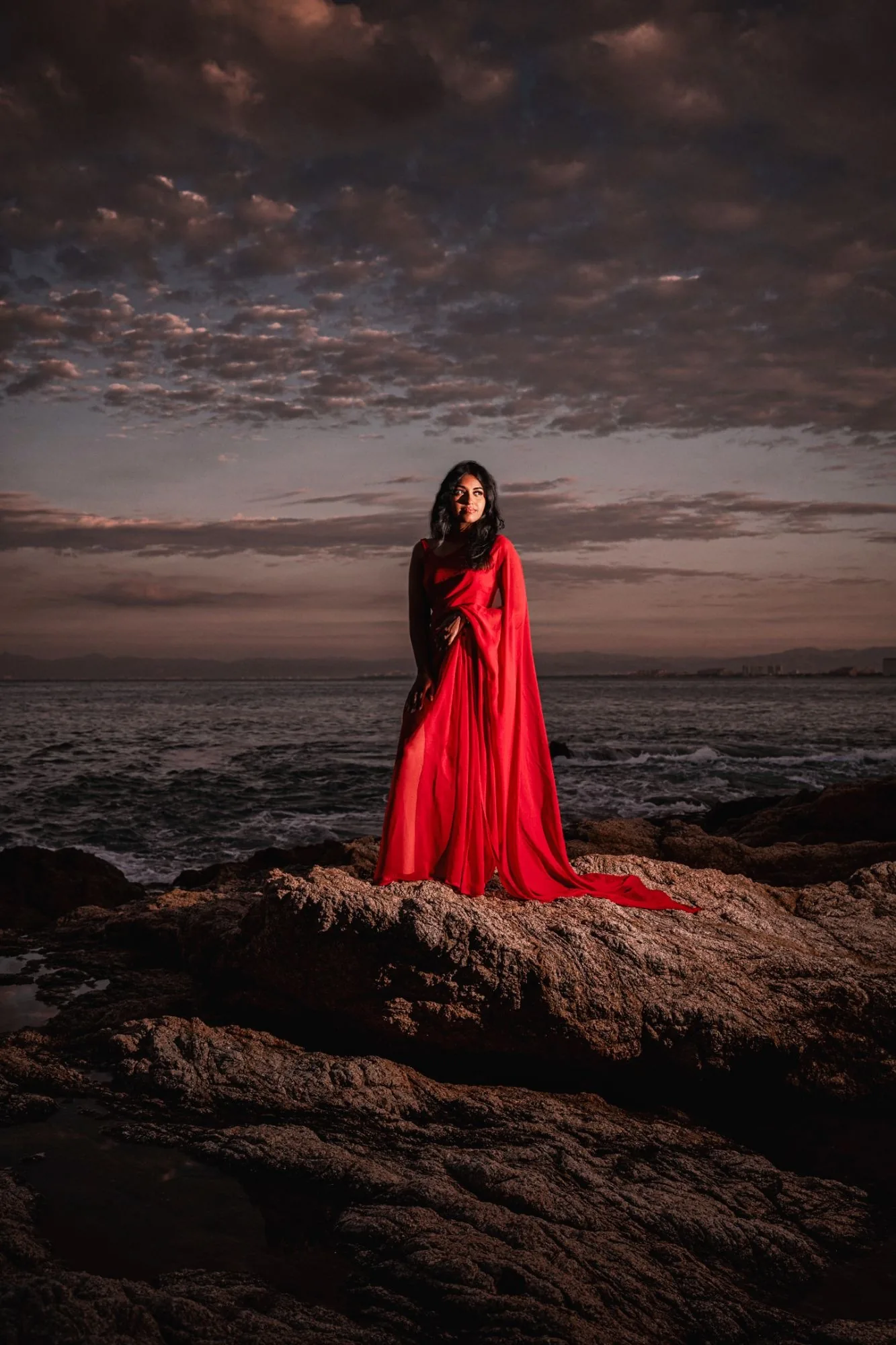 Retrato con vestido rojo sobre las rocas al anochecer